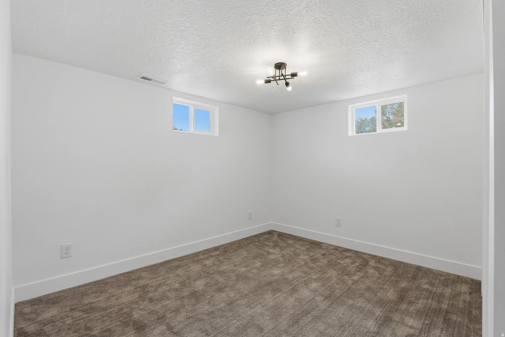 Neutral wall color with a textured ceiling, modern ceiling fixture, two windows, and patterned carpet