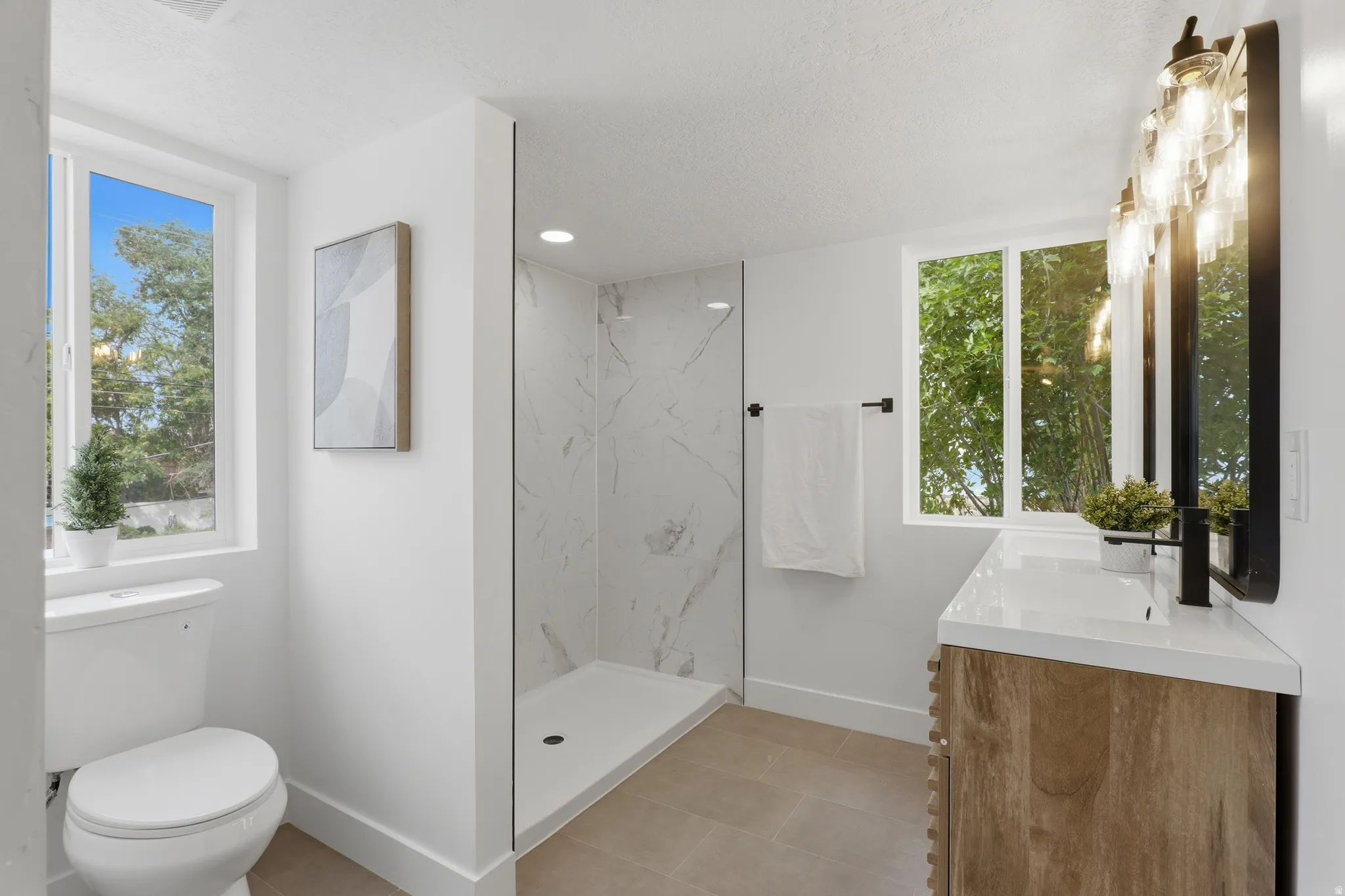 Full bathroom featuring a walk-in shower with tile surround, a single vanity with stone countertop, and two windows