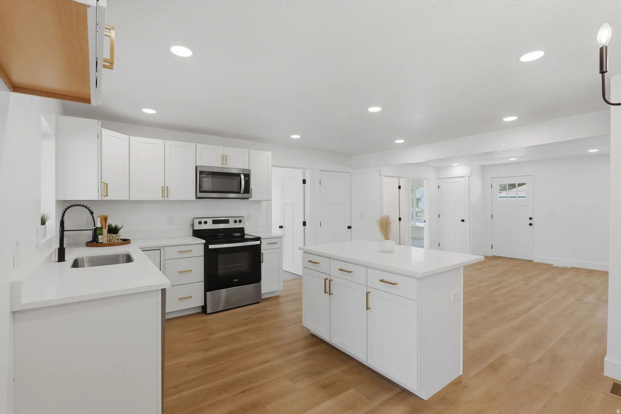 Kitchen featuring white cabinetry with gold-toned hardware, stainless steel appliances, a center island with a stone countertop, wood-finish flooring, and recessed lighting