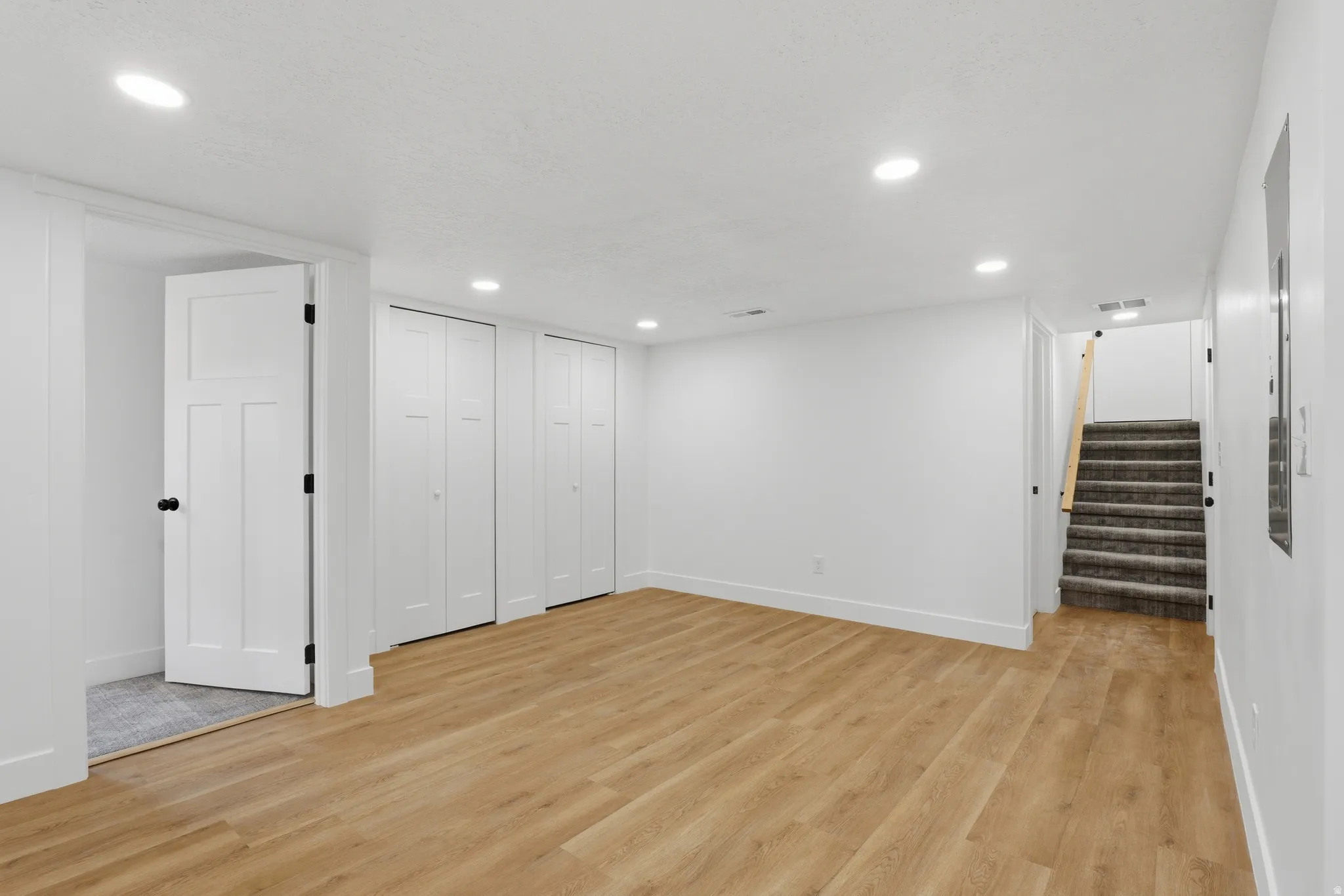 Recessed lighting, wood-finish flooring, two sets of bi-fold closet doors, white paneled interior door, and carpeted stairs with a wood handrail