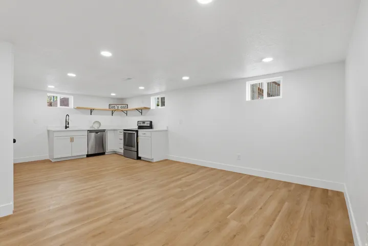 Recessed lighting, wood-finish flooring, white cabinetry with gold-tone hardware, stainless steel appliances, and white countertops