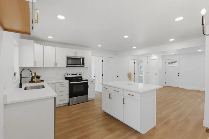 Kitchen featuring white cabinetry with gold-toned hardware, stainless steel appliances, a center island with a stone countertop, wood-finish flooring, and recessed lighting