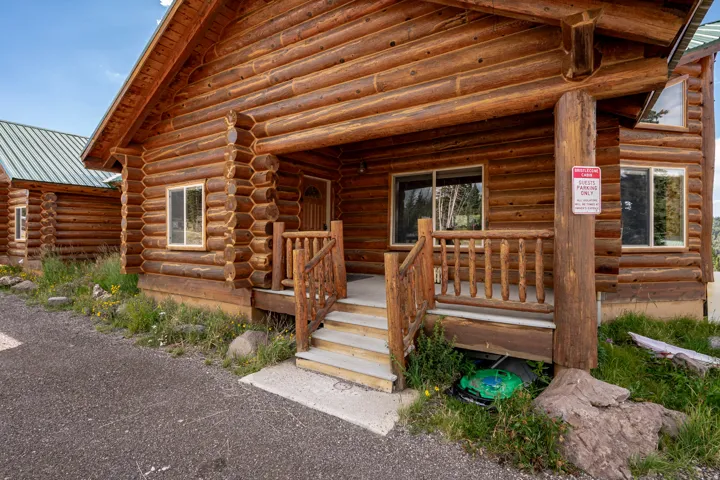 Log cabin exterior featuring a covered porch, wood railing, and concrete steps