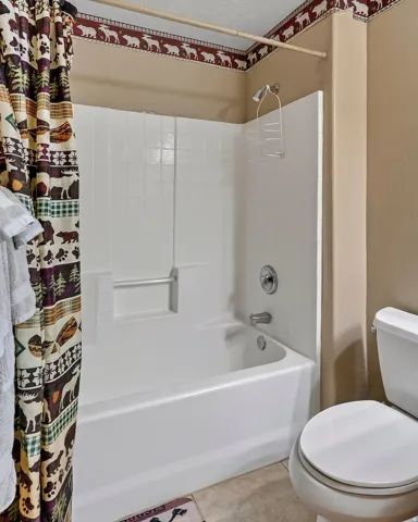 White bathtub with a chrome shower fixture, tiled shower surround, and a white toilet