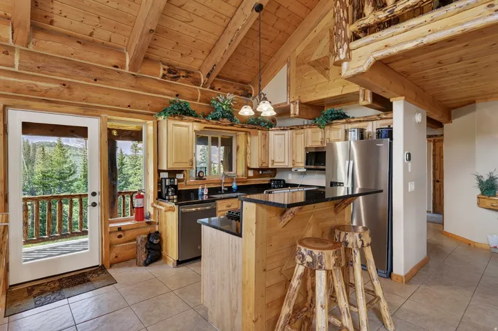 Vaulted ceilings with exposed timber beams, wood-finish cabinetry, stainless steel appliances, black countertops, and tiled flooring