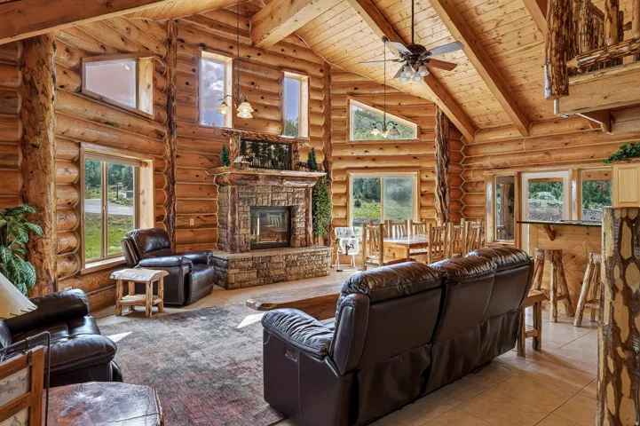 Vaulted wood-paneled ceiling, exposed wood beams, stone-faced fireplace, large windows, and tile flooring