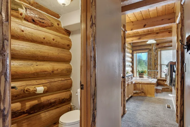 Log wall paneling, natural wood door frames, wood ceiling beams, built-in soaking tub, and vanity with integrated sink