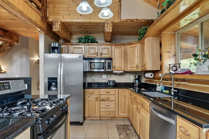 Kitchen featuring wood cabinetry, black countertops, stainless steel appliances, and a tiled floor