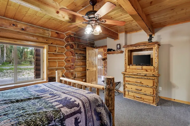 Log walls, wood-paneled ceiling with exposed beams, ceiling fan, and carpeted flooring