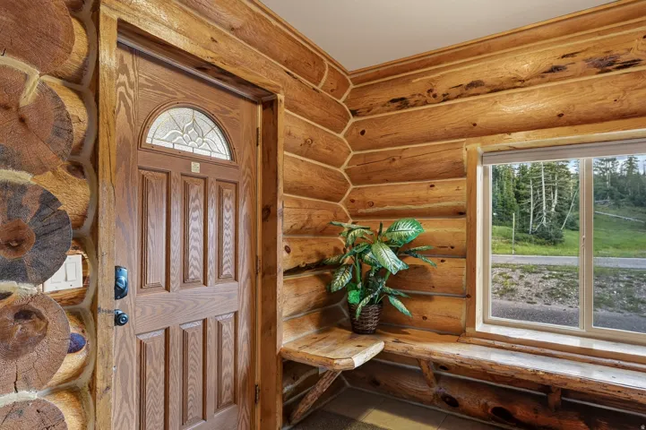 Wood-finish entry door with decorative glass insert, log-style wall construction, wood-finish built-in bench, wood-finish built-in shelf, and a large window with exterior scenery