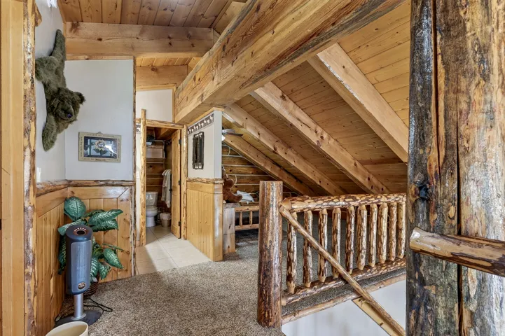 Wood-paneled walls with natural wood trim, exposed wooden beams, and a rustic wooden staircase railing