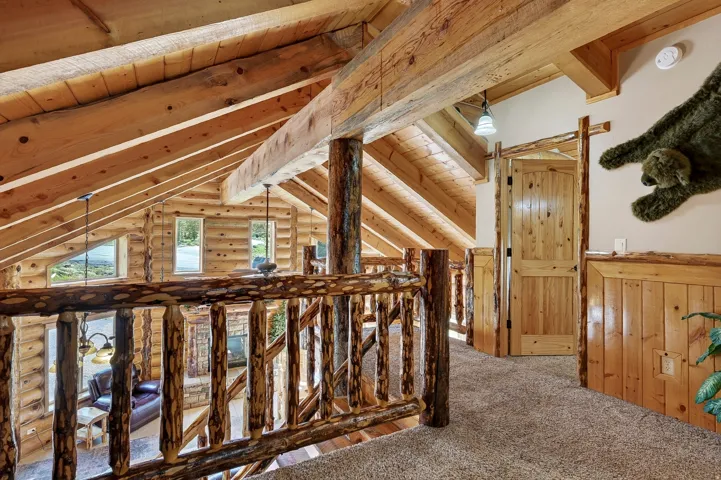 Exposed wood beam ceiling, rustic wood railing, natural wood paneling, wood plank door, and carpeted flooring