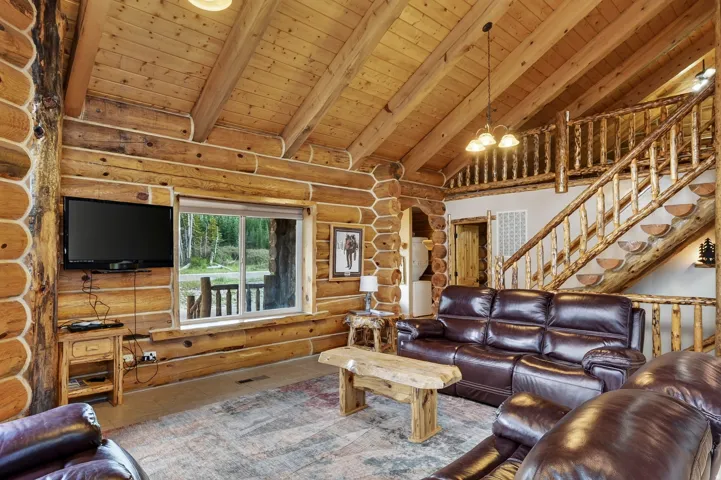 Exposed log beam construction, vaulted wood ceiling, wood-finish flooring, and a log staircase with railing