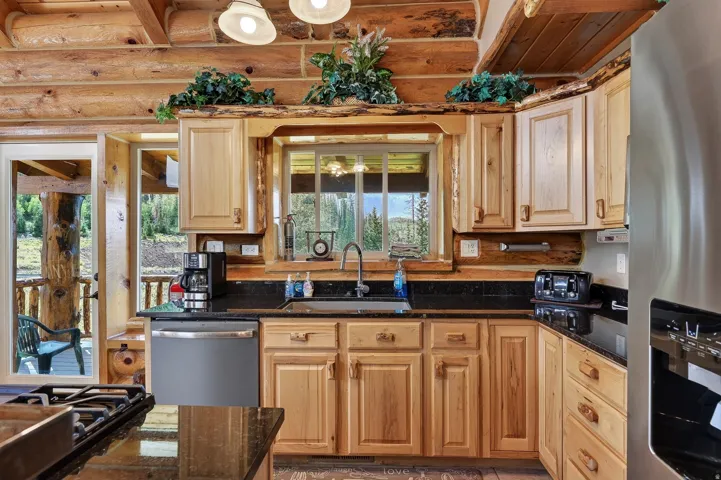 Wood-beam ceiling and walls, light wood cabinetry, black countertops, stainless steel appliances, and a built-in sink
