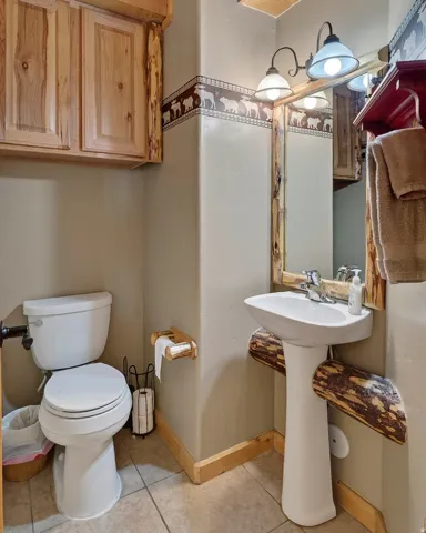 Wood-finish cabinetry, pedestal sink with chrome faucet, tiled flooring, wood-framed mirror, and rustic wall sconce lighting