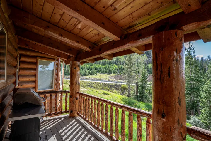 Expansive log cabin porch featuring natural wood log construction, sturdy log railing, and exposed wood ceiling beams