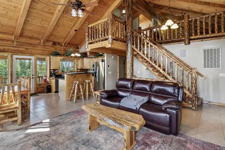Vaulted wood-paneled ceilings, open kitchen with wood cabinetry, full height breakfast bar, stainless steel appliances, and a wood-finished staircase with a landing
