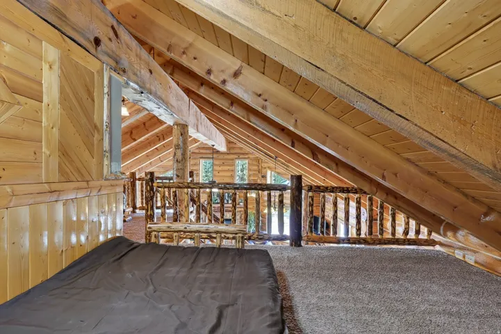 Spacious loft-style upper level featuring exposed wood beam ceiling architecture, wood-finish flooring, and carpeted sections