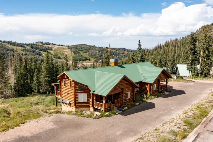 Log cabin exterior with a green metal roof, multiple covered porches, and an expansive gravel driveway