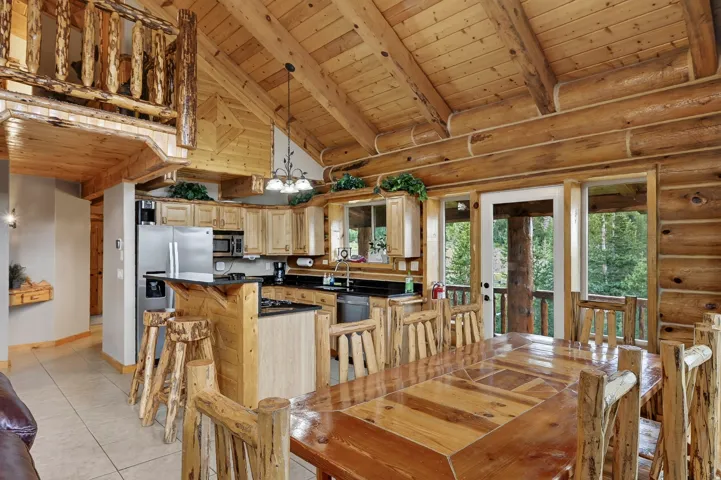 Wood-paneled vaulted ceiling, exposed log beams, full kitchen with stainless steel appliances, wood-finish cabinetry, and a loft with log railing