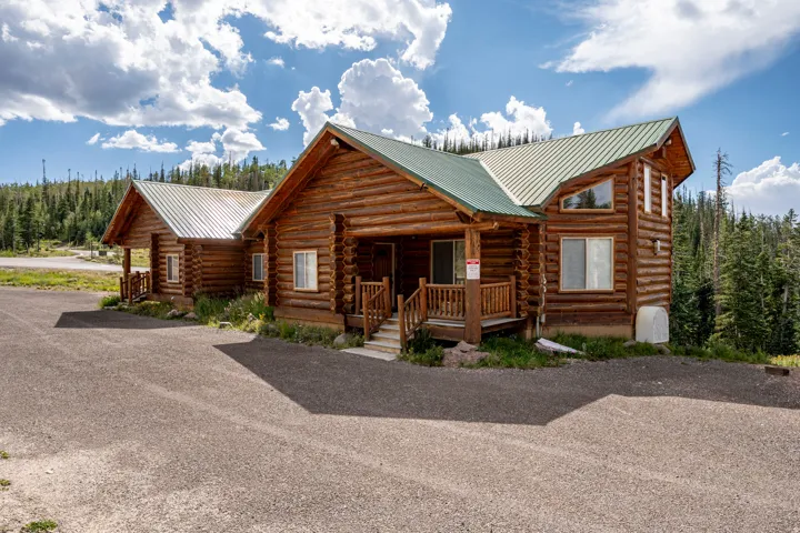 Log cabin exterior with green metal roofing, multiple pitched gables, and a gravel driveway