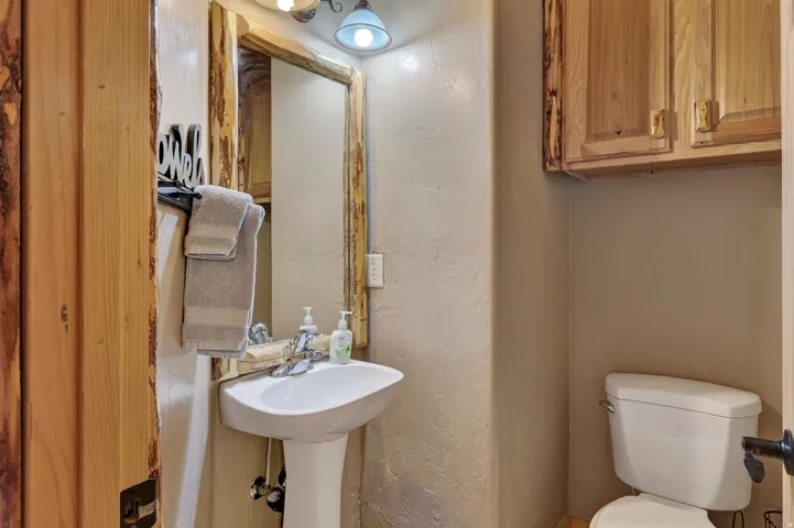 Pedestal sink with chrome faucet, wood-framed mirror, and rustic wood cabinetry