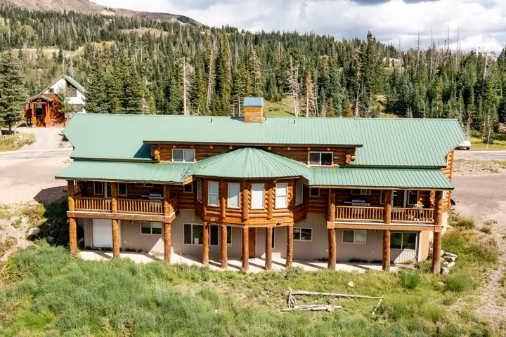 Log cabin exterior featuring a green metal roof, a wrap-around balcony, a rounded architectural element, and a stone chimney