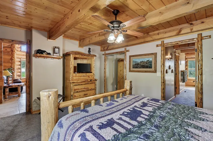 Wood-paneled ceiling with exposed beams, ceiling fan light fixture, and carpet flooring