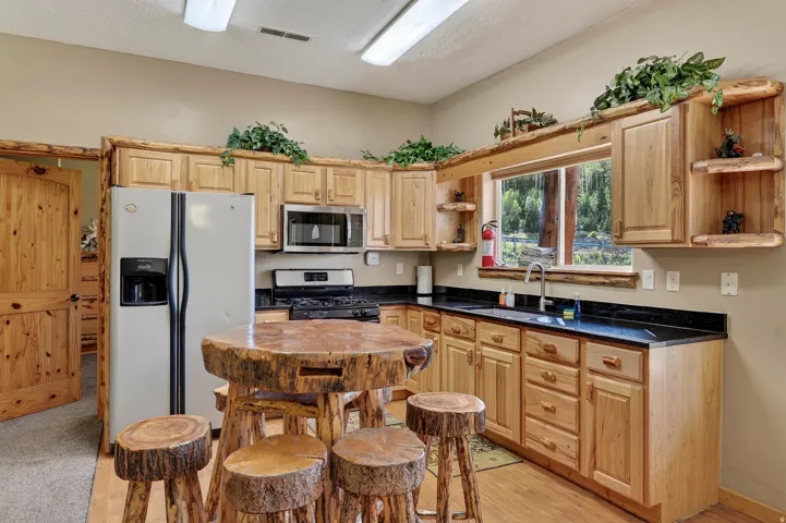 Warm wood cabinetry and stainless steel appliances define this kitchen, featuring a black countertop workspace, large refrigerator with ice and water dispensers, and gas cooktop