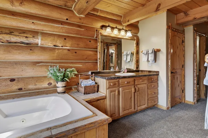 Log walls, built-in bathtub, wood-finish vanity with countertop, wood-framed mirror, and recessed lighting
