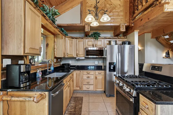 Kitchen featuring stainless steel appliances, black countertops, wood cabinetry, and a tile floor