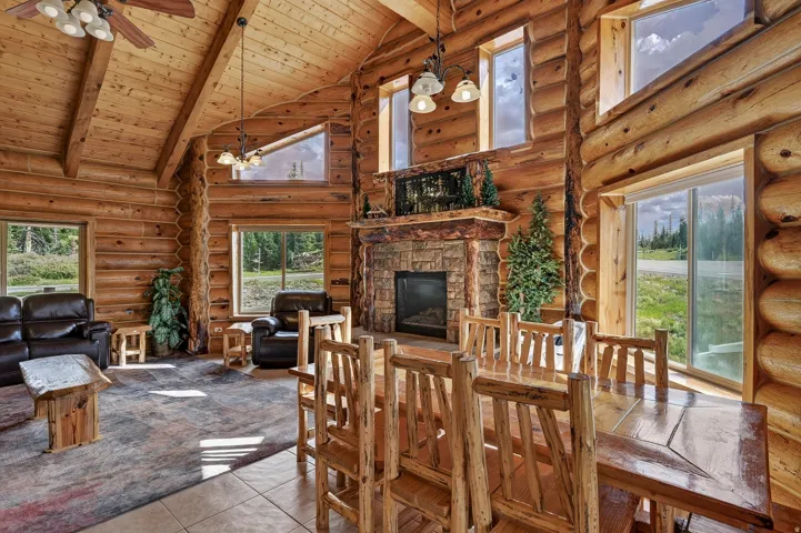 Vaulted wood plank ceilings with exposed beams, stone-clad fireplace with wood mantle, large picture windows, and wood-finish flooring