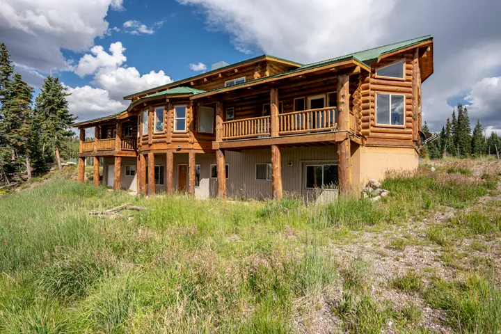 Log home exterior featuring a green metal roof, multiple levels of outdoor decking, and numerous windows