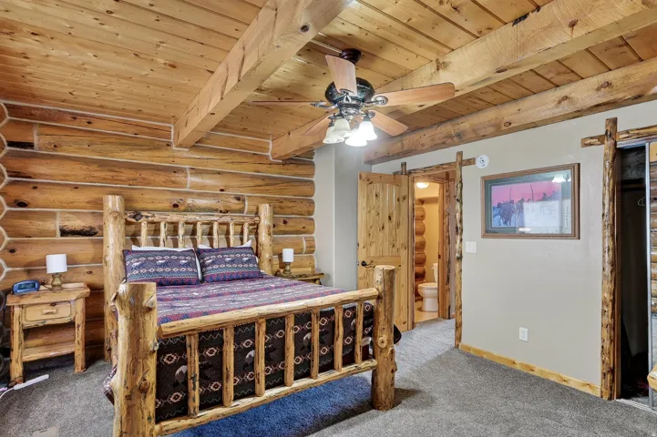 Log wall construction, wood-finish plank ceiling, exposed wood beams, and a ceiling fan with light fixture