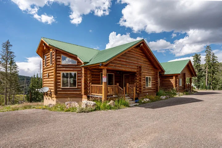 Log cabin exterior with a green metal roof, multiple windows, and a raised covered porch