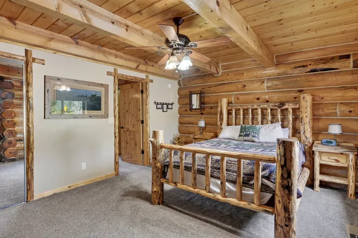 Exposed log walls, natural wood-paneled ceiling with exposed beams, wood-finish interior doors, and a ceiling fan with light fixture