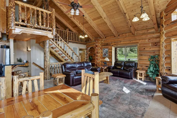 Vaulted wood-paneled ceiling, exposed wooden beams, natural log walls, wooden staircase with log railings, and a loft with log railing