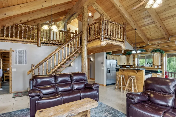 Vaulted wood-paneled ceiling, exposed wood beams, wood staircase with log railing, open-concept kitchen with wood cabinetry, and stainless steel appliances