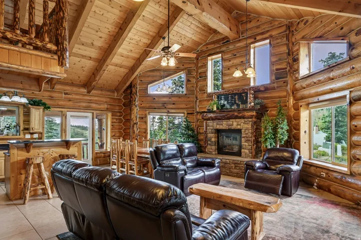 Vaulted wood-paneled ceiling with exposed beams, stone fireplace, wood-finish flooring, and a log-style banister