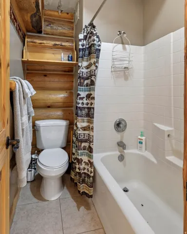 Bathroom featuring a wood-panel accent wall with built-in shelving, a white porcelain toilet, and a white tile-surround bathtub with a shower fixture