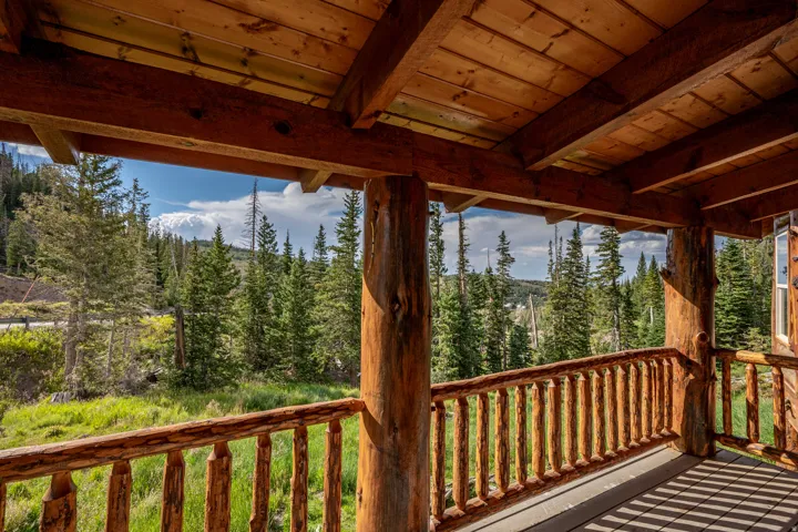 Expansive wooden deck featuring rustic log railings and support beams, a wood-plank ceiling, and a natural forested backdrop