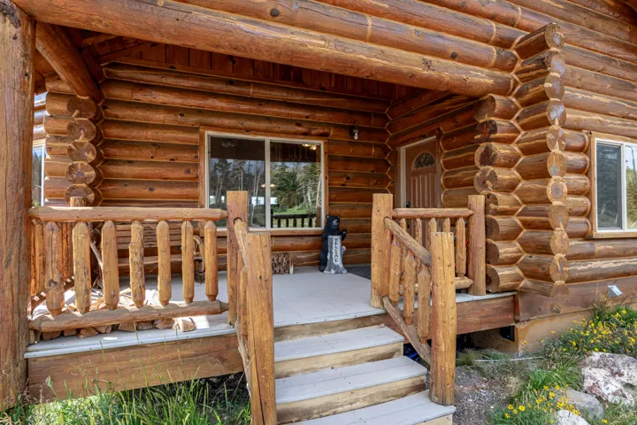 Log construction exterior featuring a covered porch, wood railing, and a multi-pane entry door