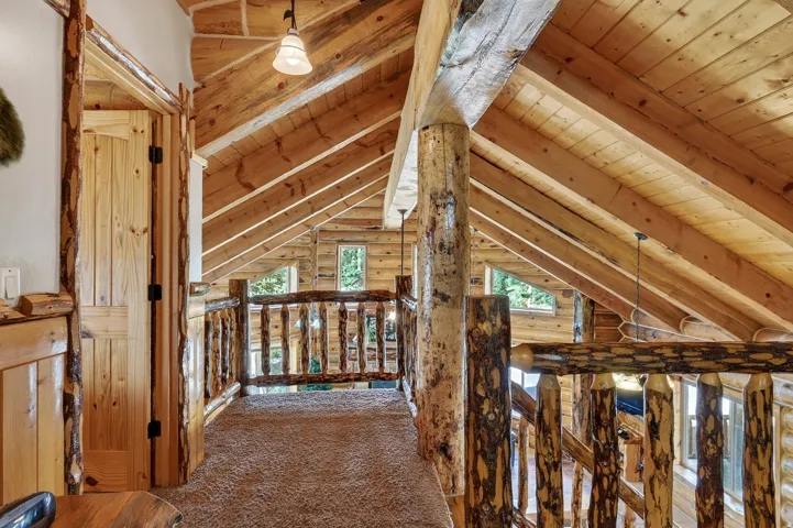 Exposed wood beam ceiling, rustic wood log railing, wood-finish door, carpeted flooring, and a pendant light fixture