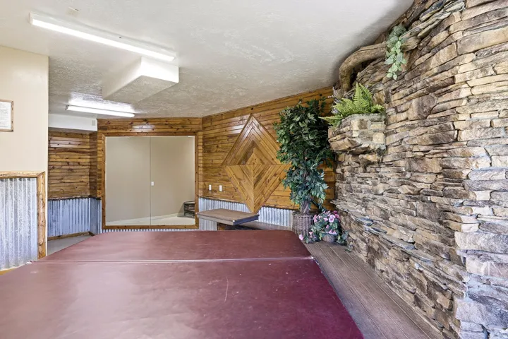 Indoor pool area featuring a stone accent wall, wood-paneled walls, corrugated metal wainscoting, and fluorescent lighting