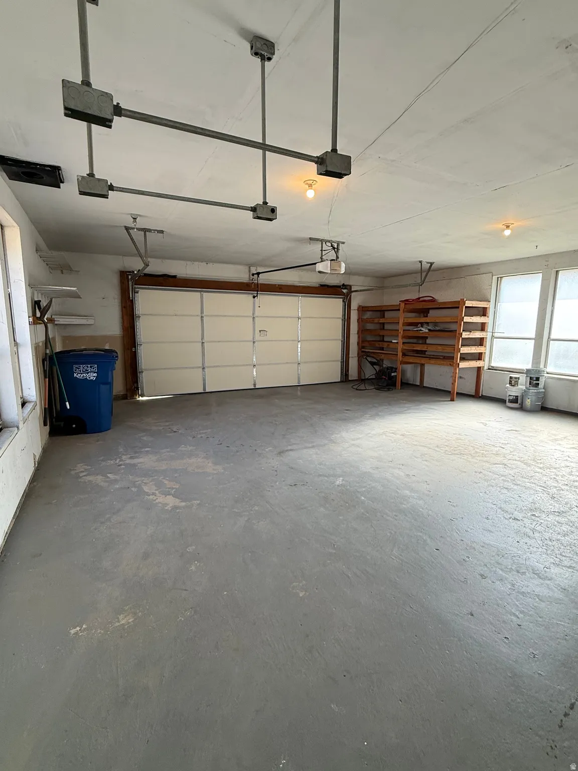 Attached garage with an overhead door, concrete flooring, built-in shelving, and multiple windows