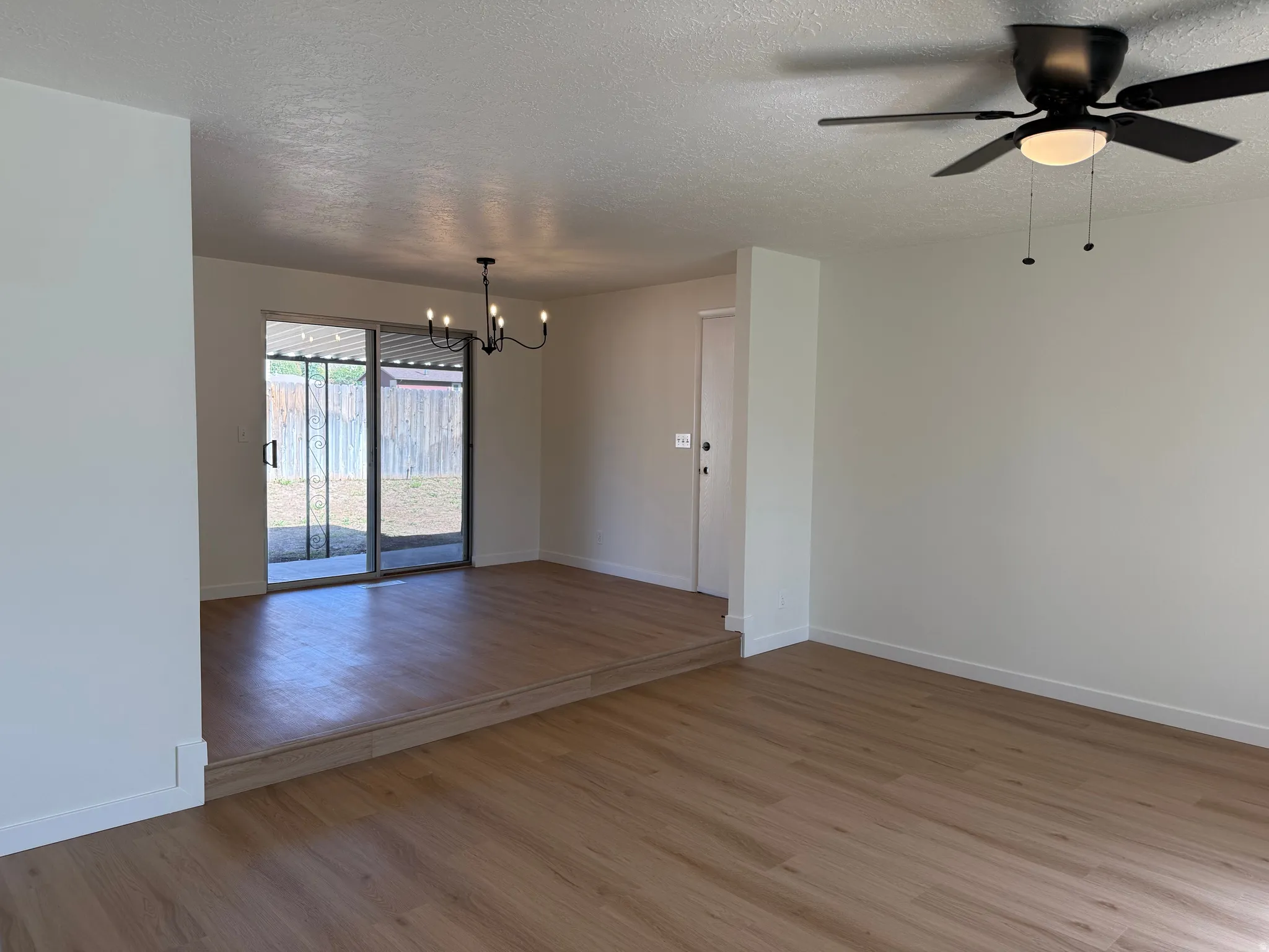 Wood-finish flooring throughout, sliding glass door with screen, multi-light chandelier, and ceiling fan with integrated lighting