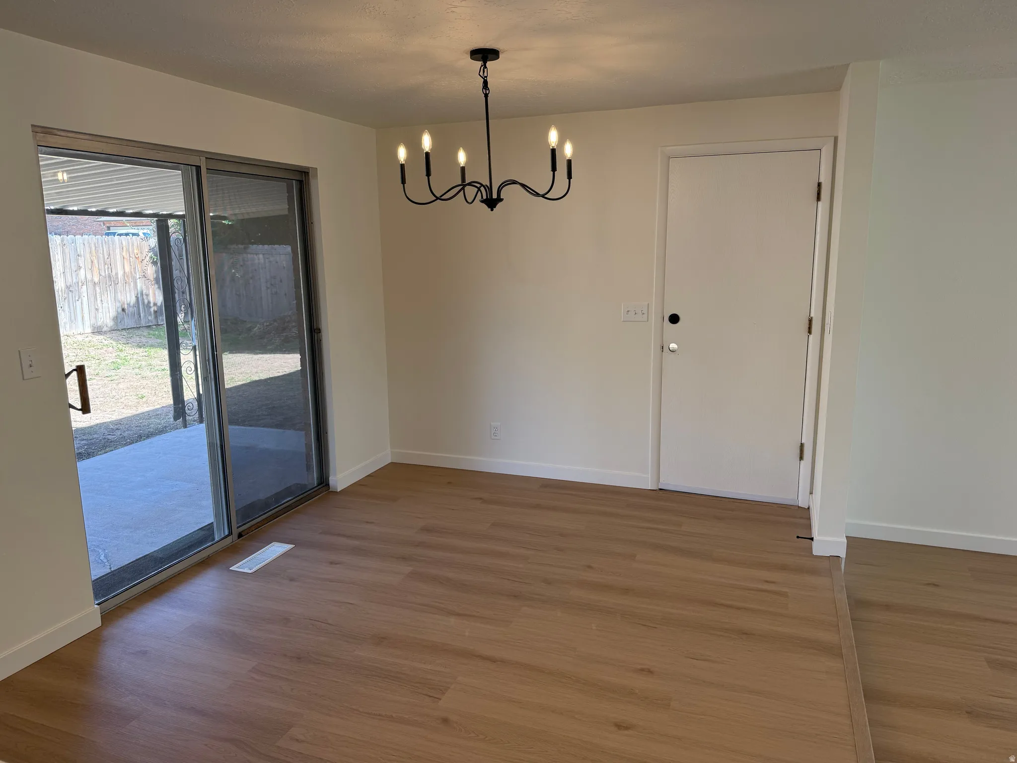 Wood-finish flooring, sliding glass door, patio with concrete surface, black chandelier, and white interior walls