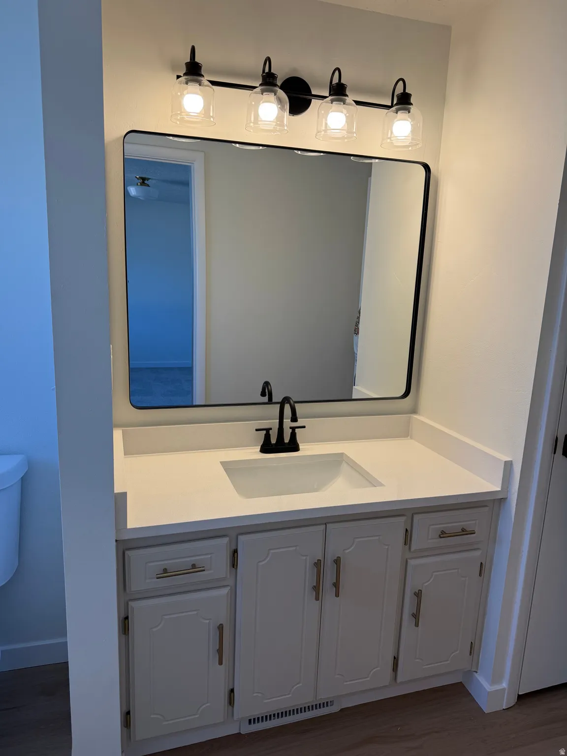 White vanity with gold-tone hardware, rectangular undermount sink, matte black faucet, and coordinating black-framed mirror