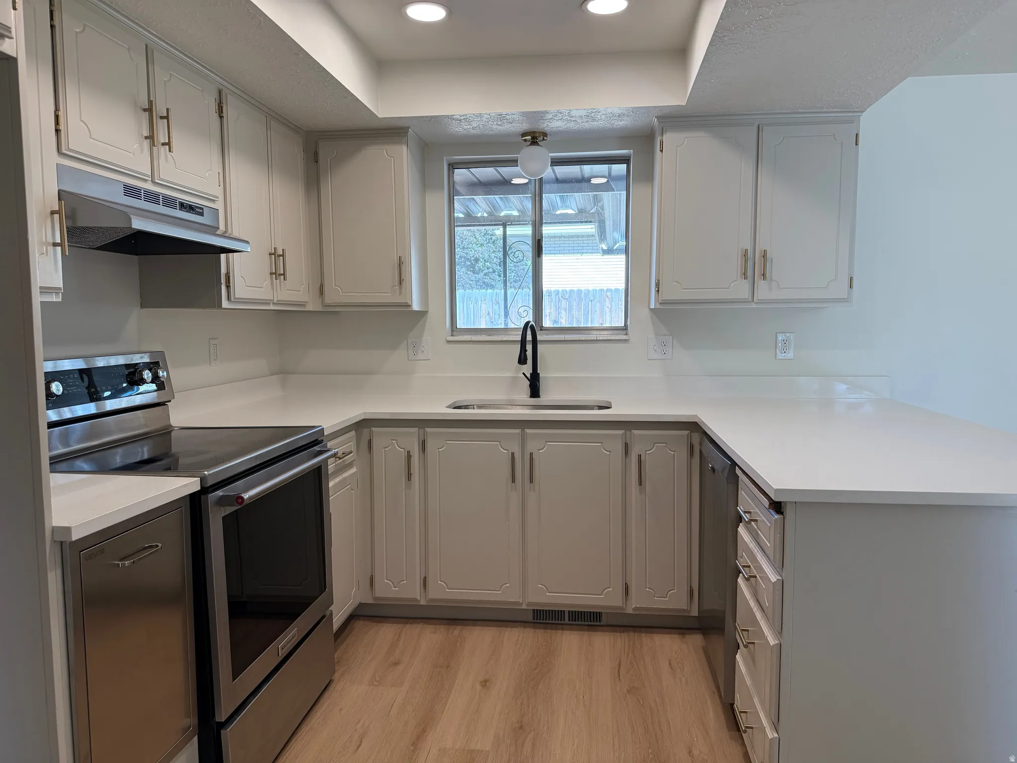 Kitchen featuring white cabinetry, light-toned countertops, stainless steel appliances, and wood-finish flooring