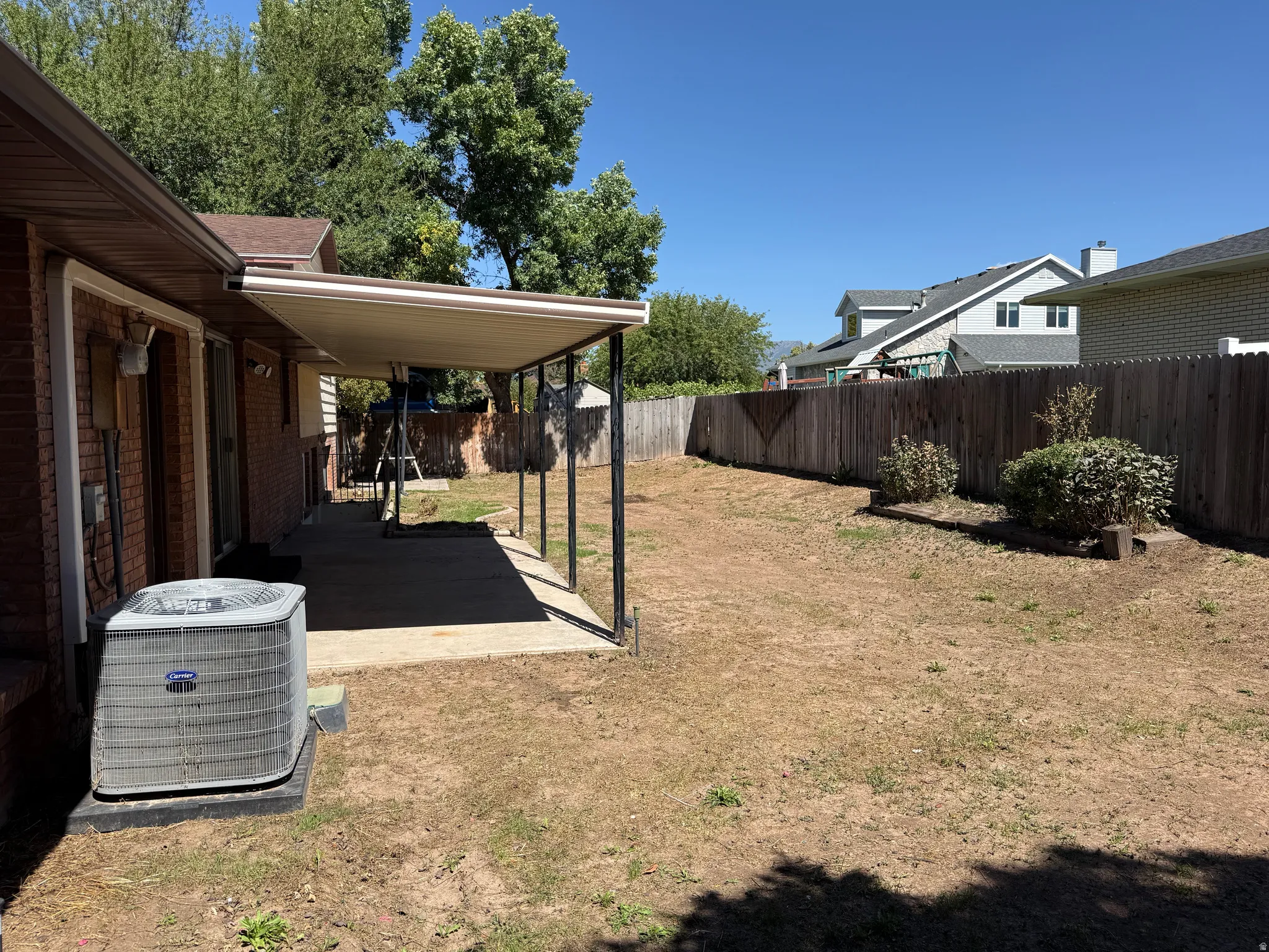 Covered patio with concrete flooring, brick exterior, and a wood privacy fence
